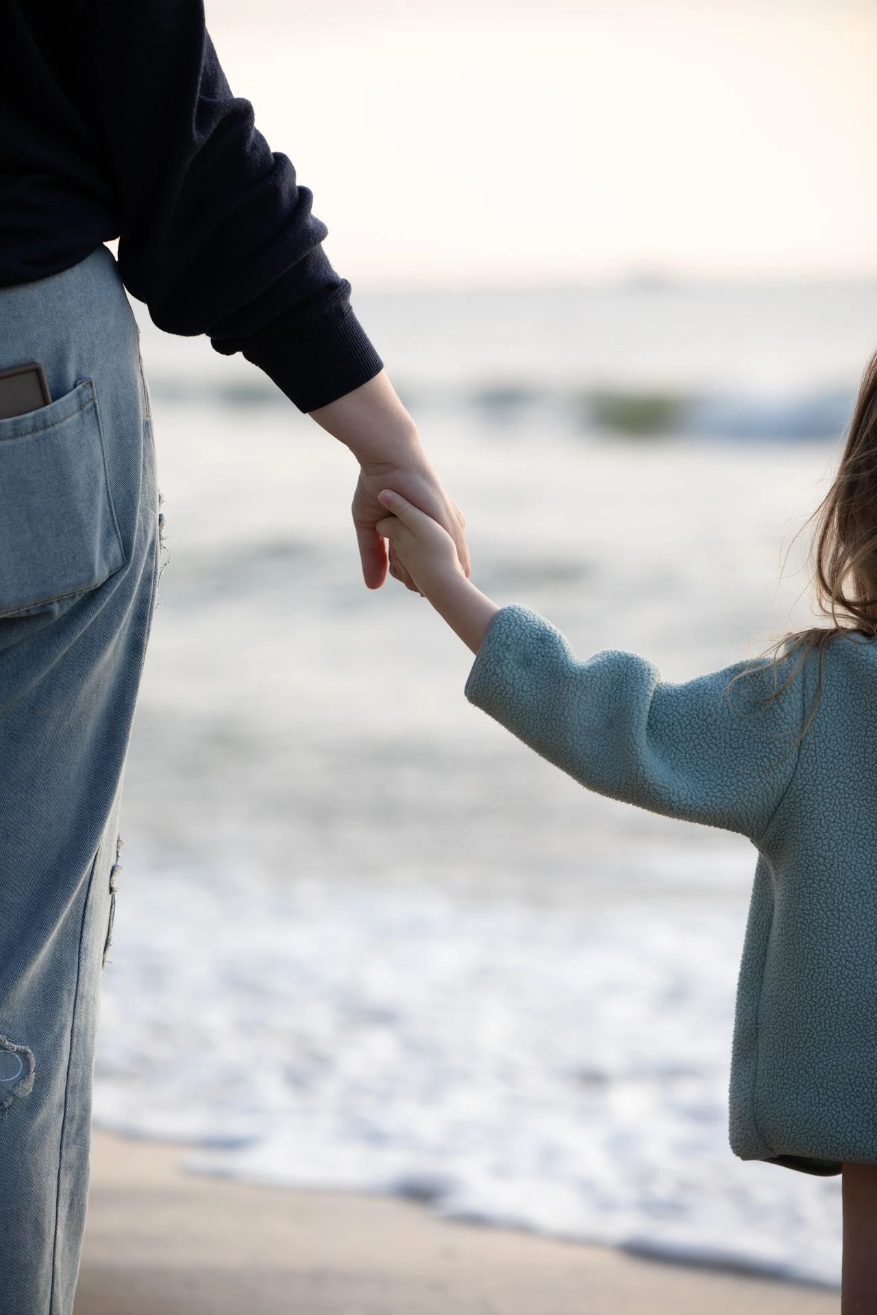 Parent and child holding hands by ocean